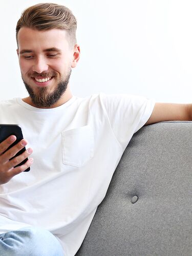 Mann auf Sofa sitzend lächelt auf sein Smartphone. 