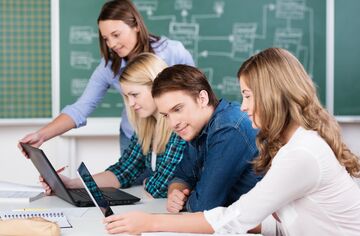 Vier junge Studierende an einem Schreibtisch auf Laptops schauend